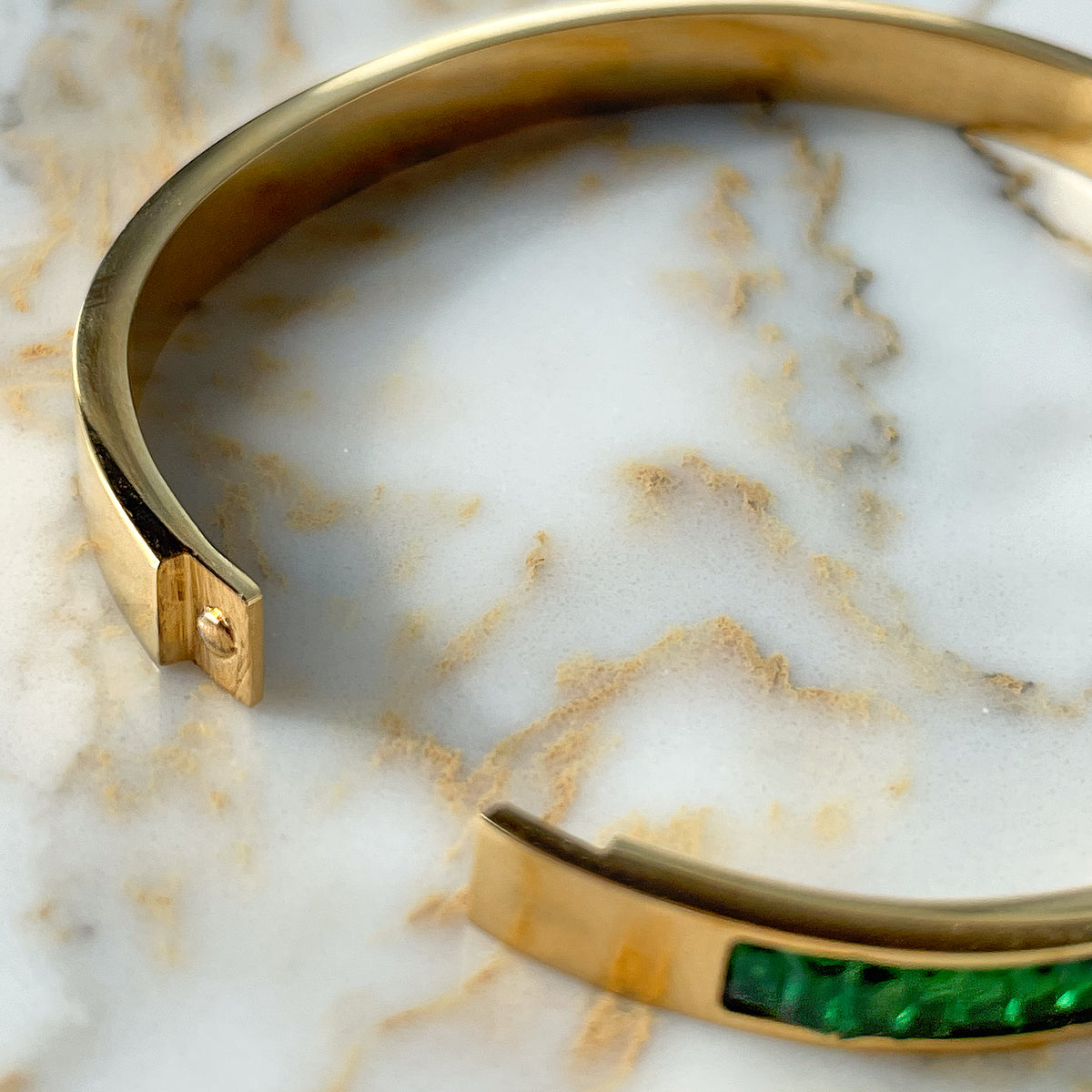 Open view of the gold-plated bangle bracelet showing the side clasp mechanism and green crystal details.