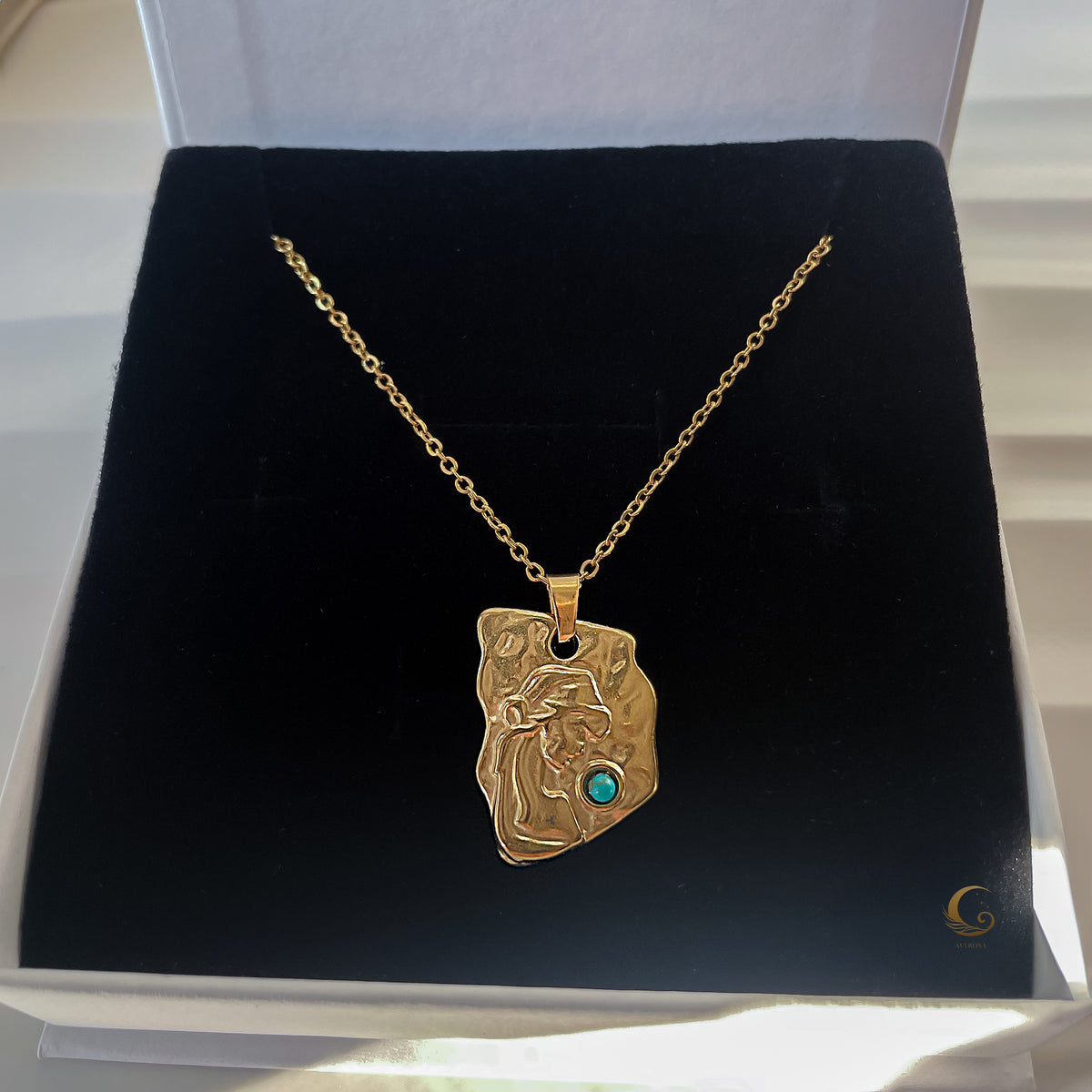 Gold necklace with a pendant on a black cushion inside a jewelry box