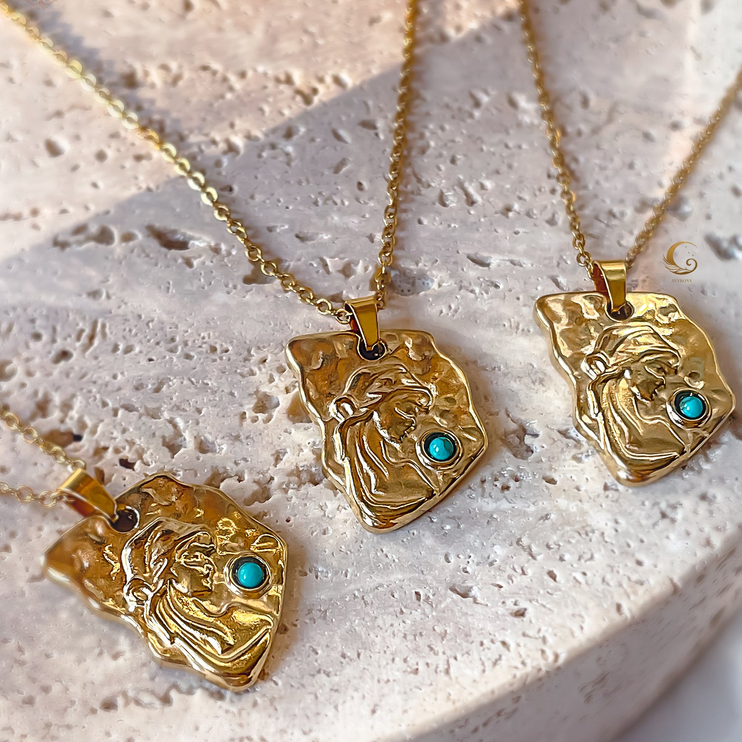 Three gold necklaces with face-shaped pendants and turquoise stones on a textured white surface.