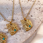 Gold necklaces with face-shaped pendants and turquoise stones on a textured surface