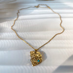 Gold necklace with a pendant featuring a face design and a blue gemstone on a white surface.