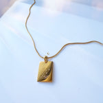 Gold necklace with a rectangular pendant on a light blue background