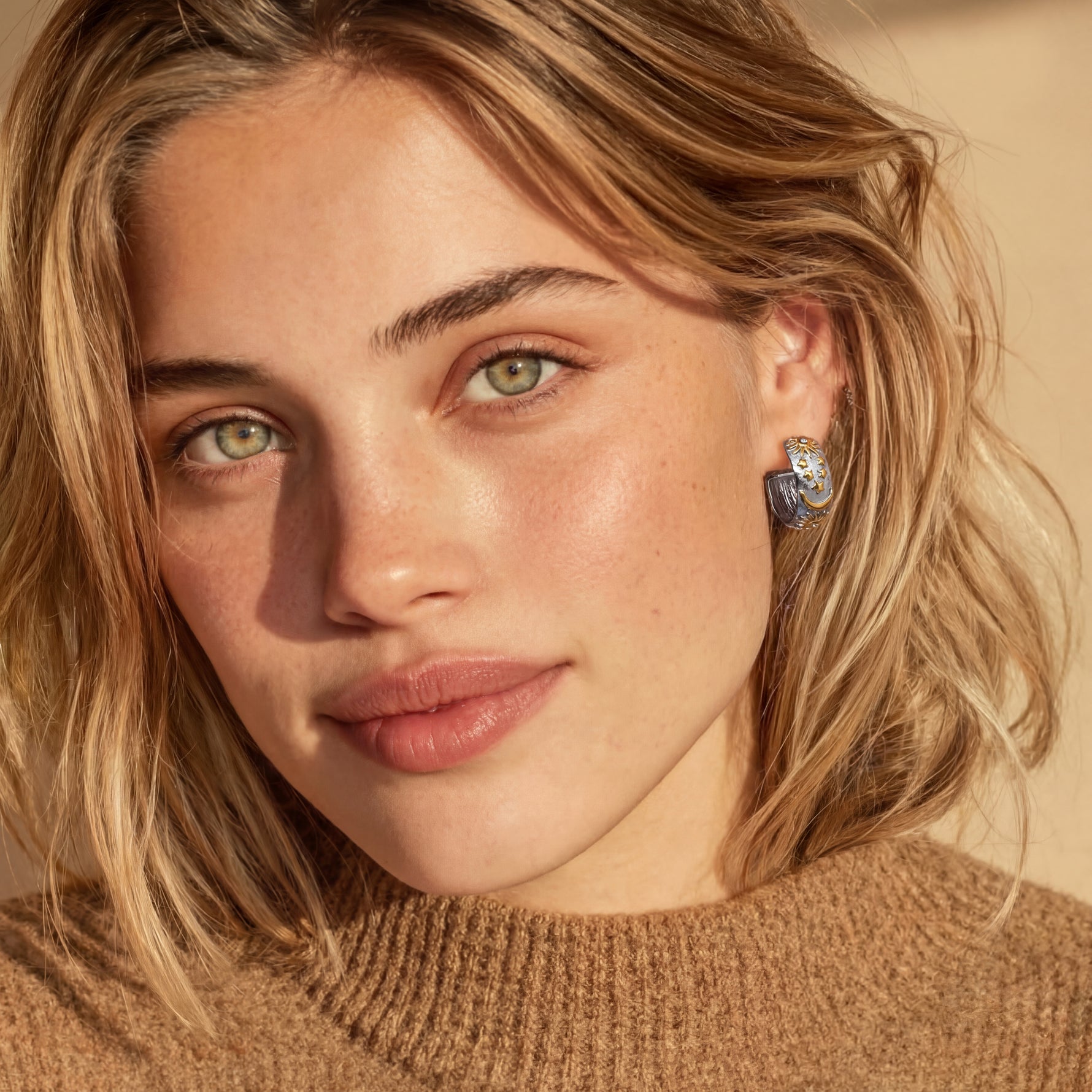 Close-up of a person with blonde hair wearing a brown sweater and earrings.