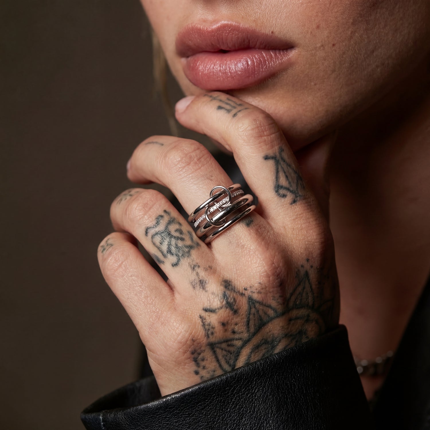Close-up of a hand with tattoos wearing multiple rings on a dark background