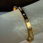 A gold bracelet with a sun motif and small cubic zirconia stones, displayed on a smooth, light-colored tube.