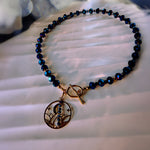 A beaded necklace with dark blue faceted beads and a gold-toned circular pendant featuring a crescent moon and stars, resting on a white textured surface.