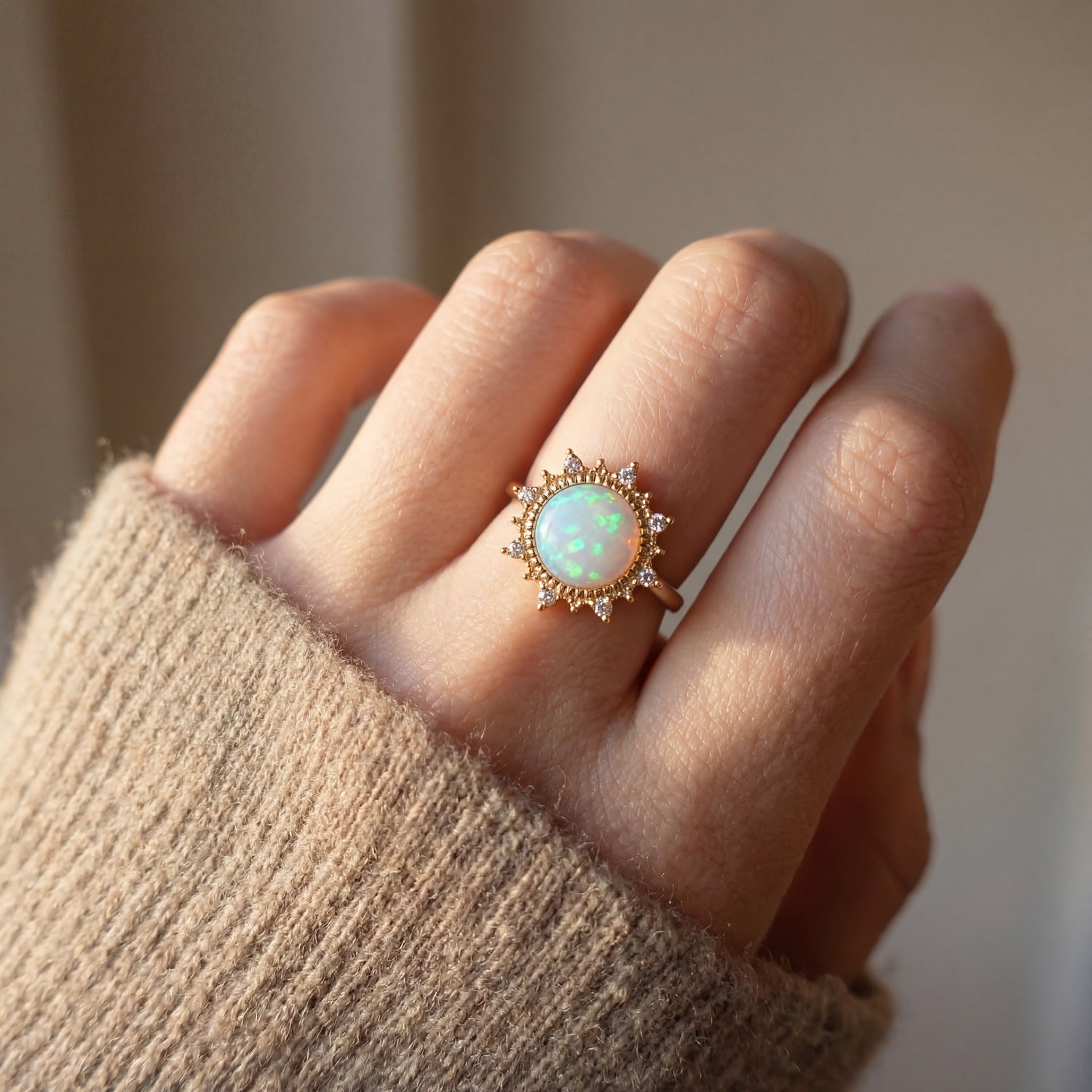 Hand wearing a ring with an opal stone and gold accents, against a neutral background.