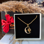 Gold necklace with moon and star pendant on a black display card, next to a gift box with a red bow.