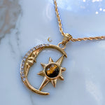 Gold necklace with moon and sun pendant on a marble surface