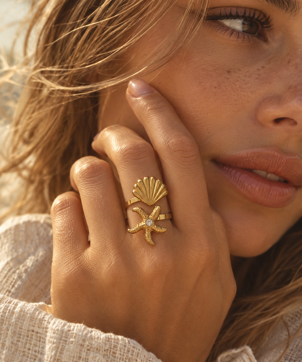 A close-up lifestyle shot of a woman wearing a gold ring featuring a starfish and a scallop shell design with a small clear center stone.
