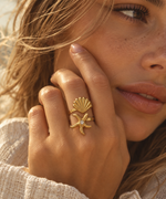 A close-up lifestyle shot of a woman wearing a gold ring featuring a starfish and a scallop shell design with a small clear center stone.