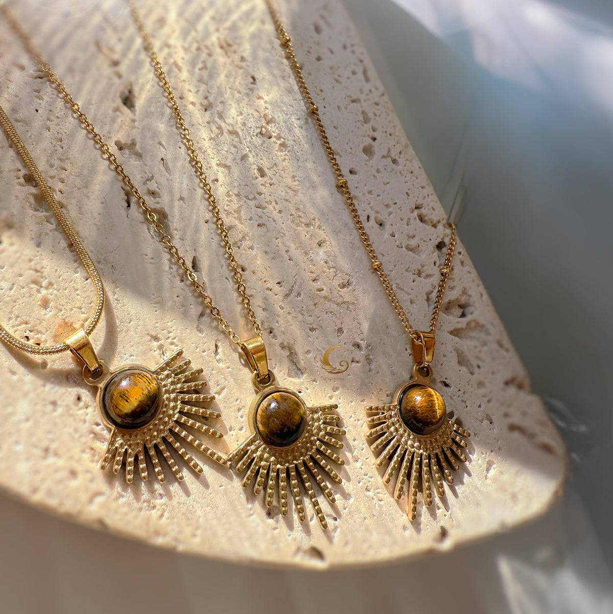 Three gold necklaces with sunburst pendants on a textured stone surface