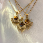 Three gold necklaces with sunburst pendants on a light background