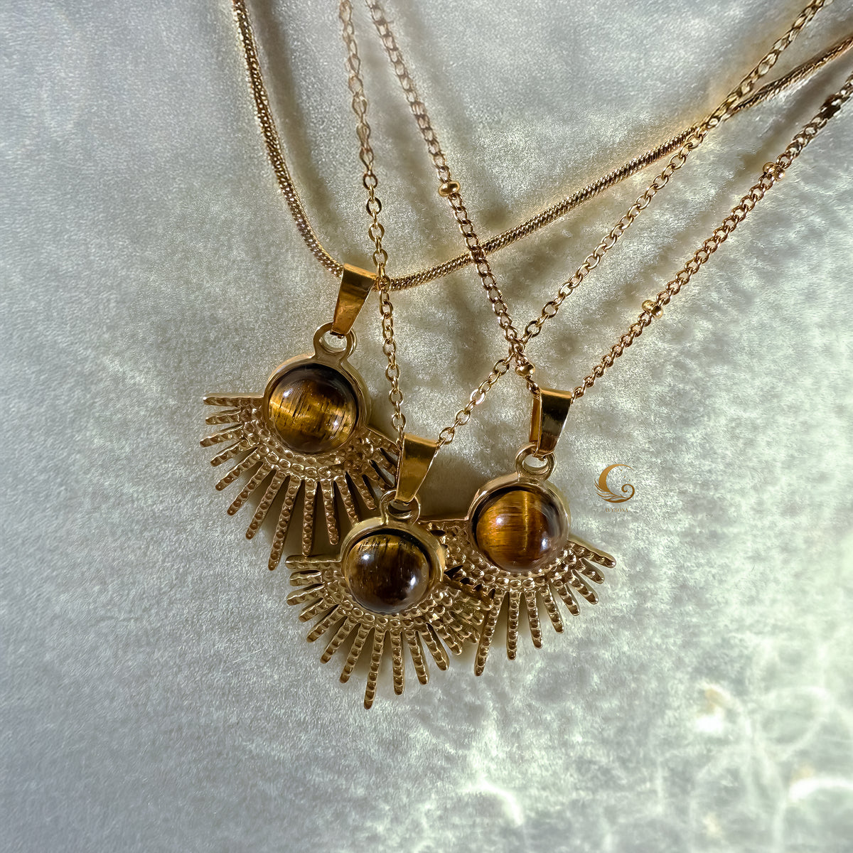 Three gold necklaces with tiger's eye pendants on a light gray background