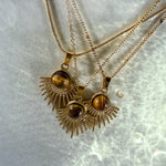 Three gold necklaces with tiger's eye pendants on a light gray background