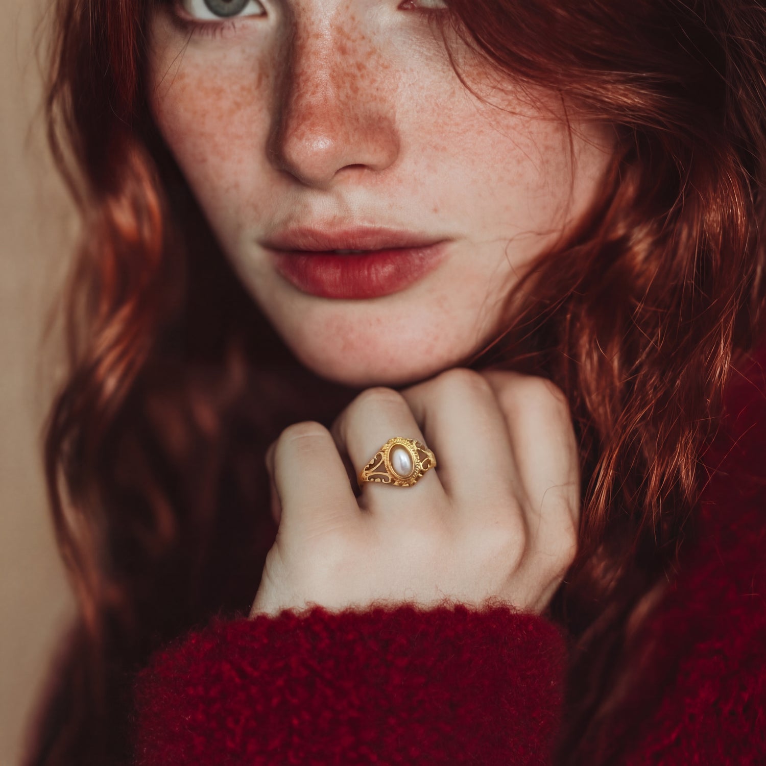 Close-up of a person with red hair wearing a gold ring, with a blurred background.