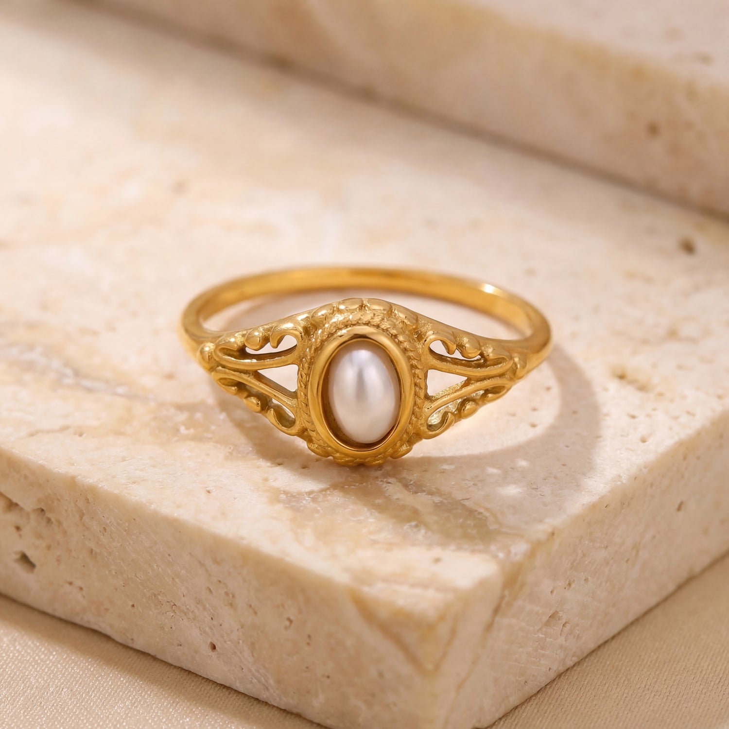 Gold ring with a pearl on a beige stone surface