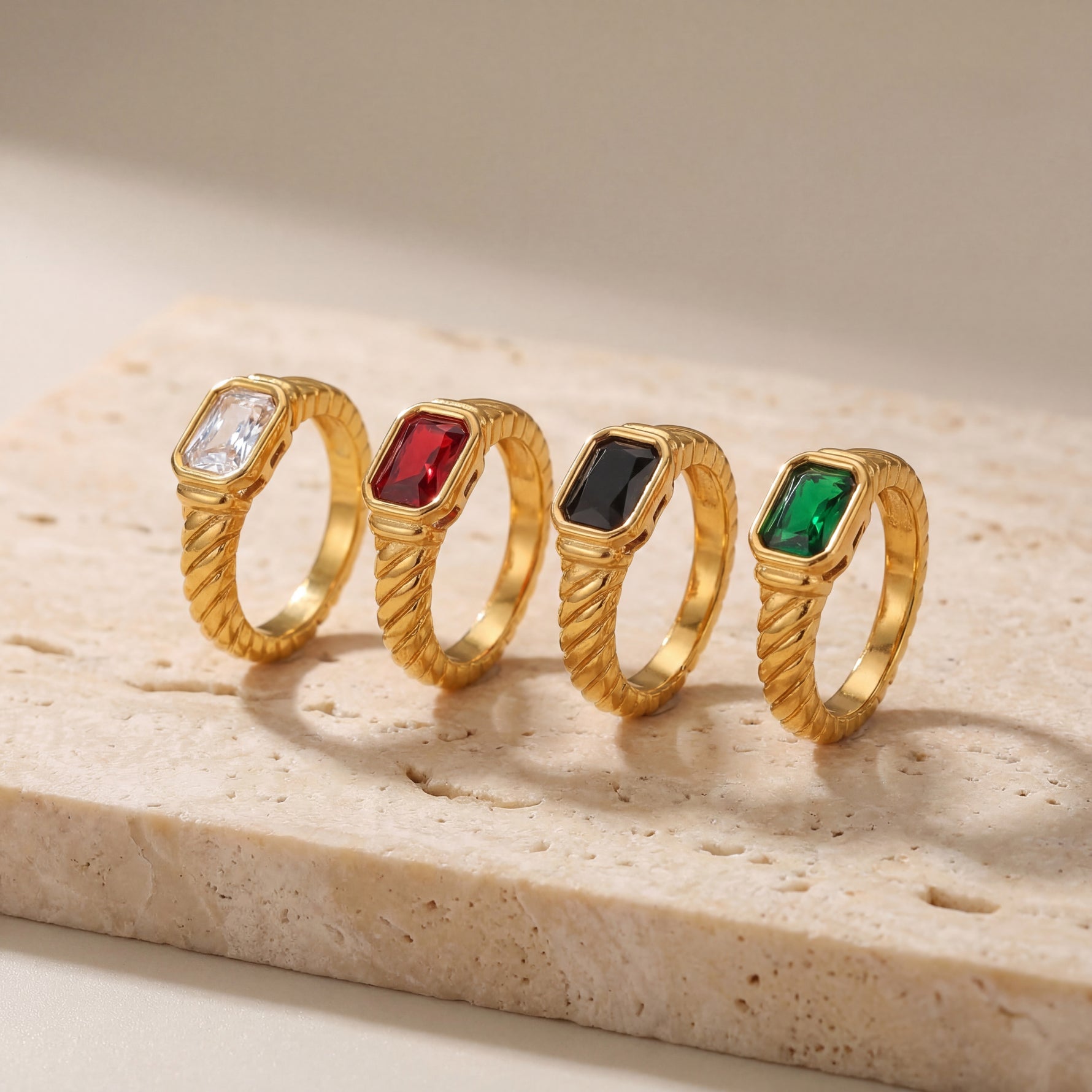 Four gold rings with colored gemstones on a stone surface