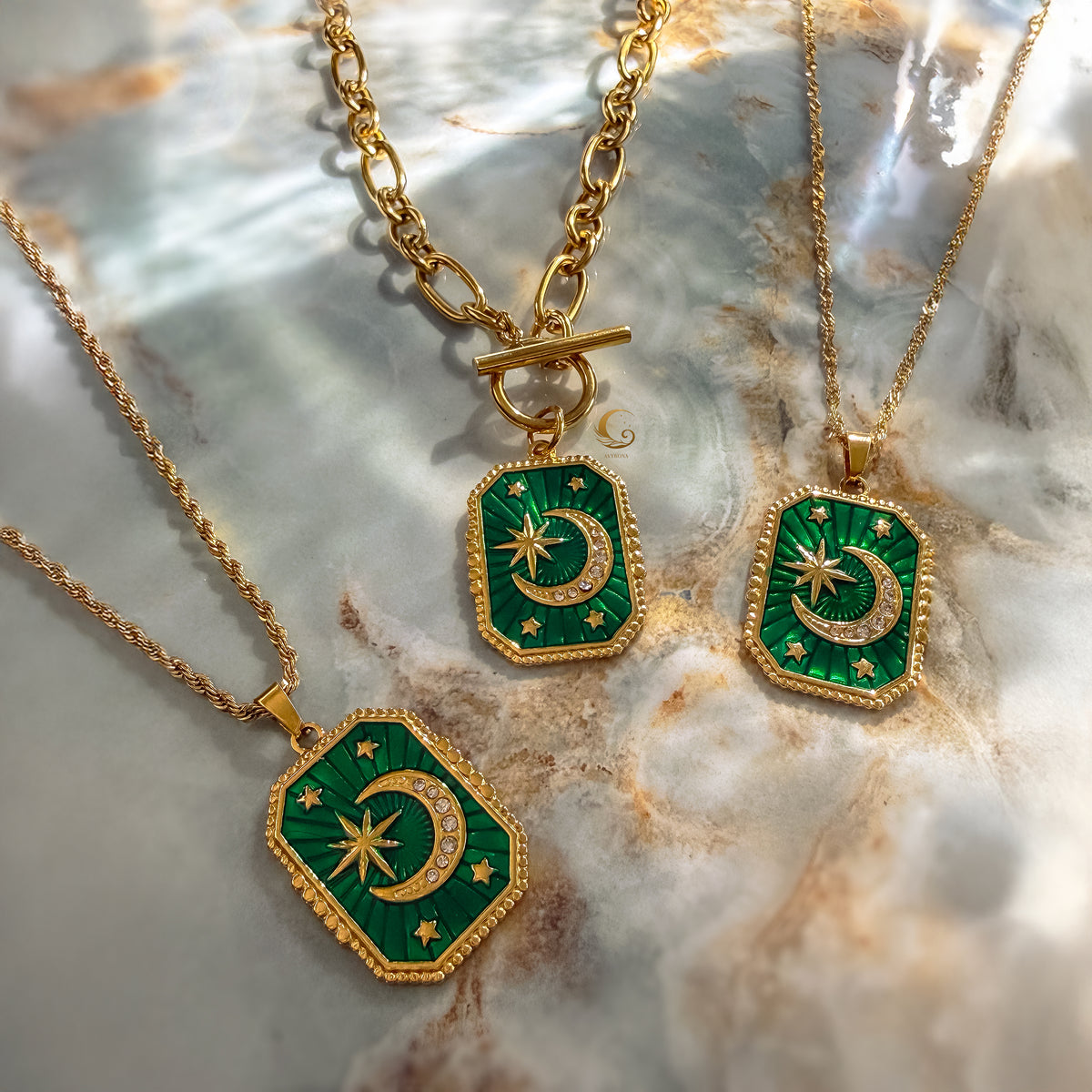 Two gold necklaces with green pendants featuring celestial designs on a marble surface.