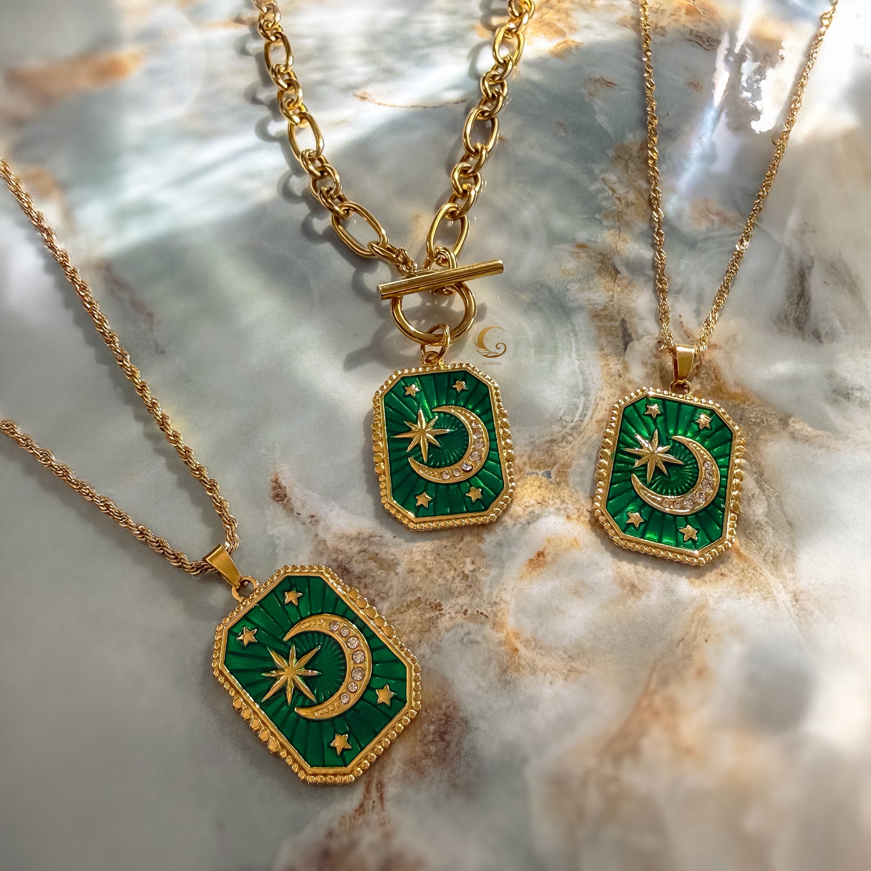 Two gold necklaces with green pendants featuring celestial designs on a marble surface.