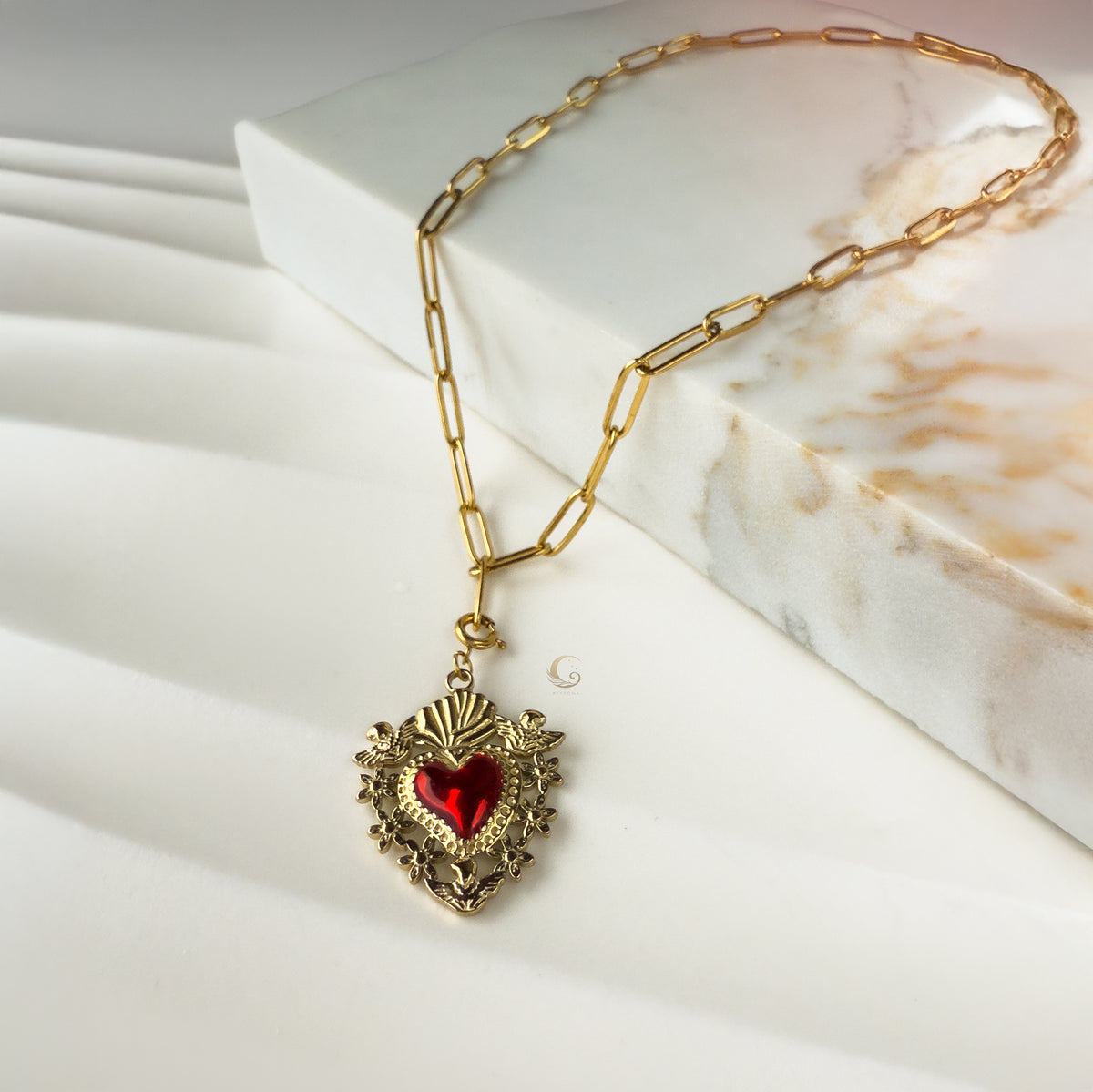Amara Sacred Heart necklace displayed on marble background with red enamel heart charm.