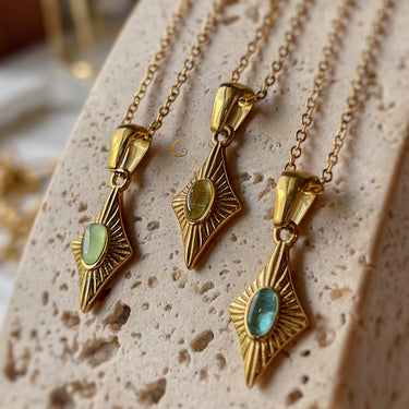 Three gold cat eye necklaces with green, yellow, and blue stones displayed on textured stone background