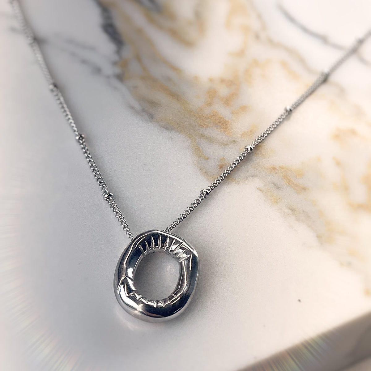  Close-up of single silver balloon-style letter “O” necklace on chain, resting on warm-toned marble.