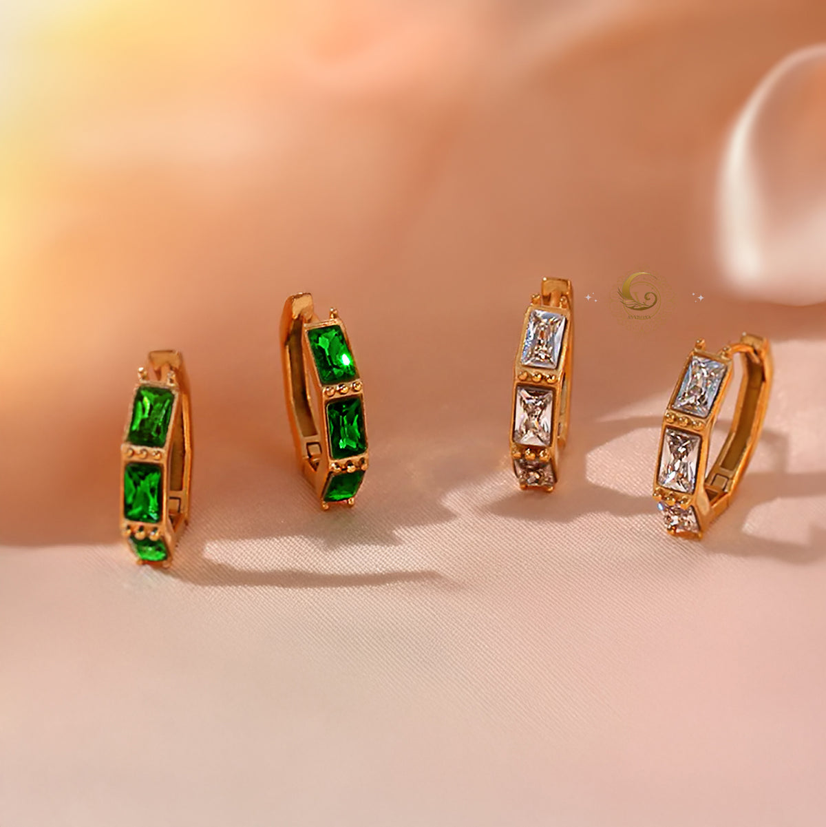 Camila earrings in both green and clear zircon versions placed on a silky beige fabric background