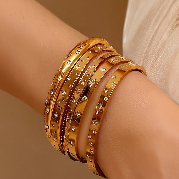 Elegant open cuff bracelet with evenly spaced star engravings and small zirconia stones, placed on warm-toned marble.