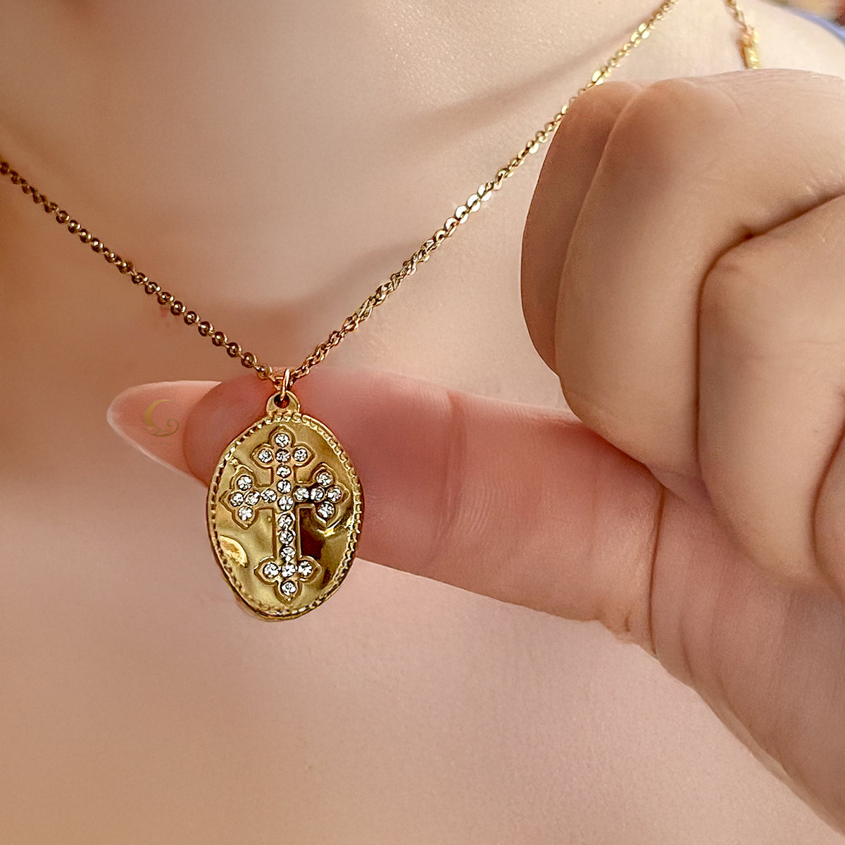 Celestia gold cross necklace gently held between fingers to show pendant size and sparkle against skin.