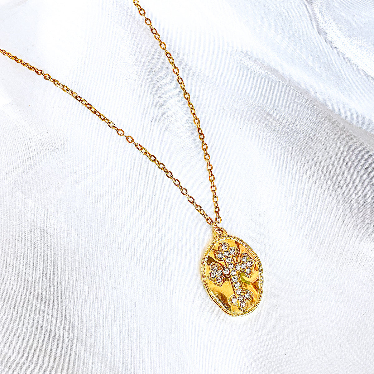 A single Celestia cross medallion necklace with cubic zirconia, elegantly displayed on white fabric.