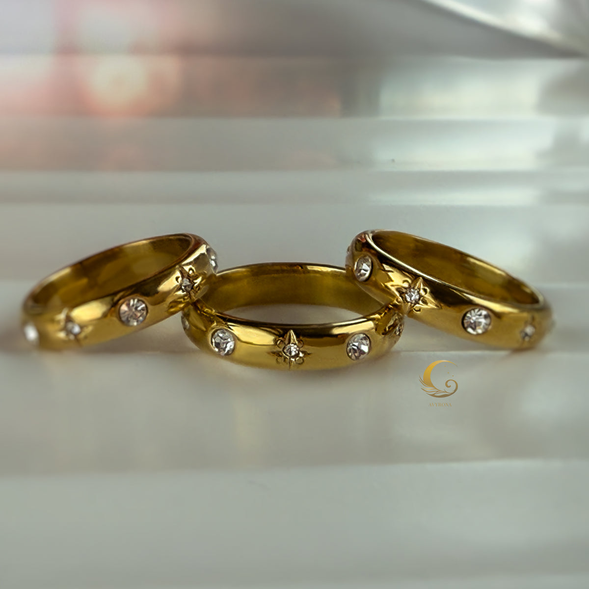 Trio of Celestial Glow rings with crystal and star details on soft white surface