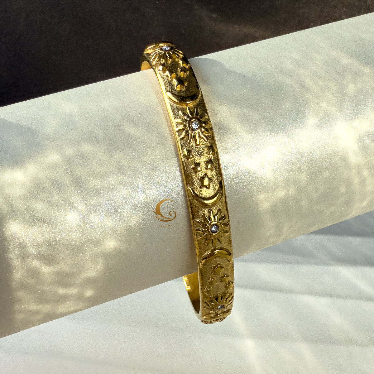 Overhead view of the gold celestial bracelet laid on a curved display, emphasizing engraved sun and star details with light reflection.