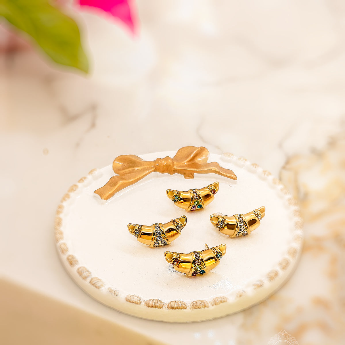 Set of four gold croissant earrings arranged with a golden ribbon on a white plate