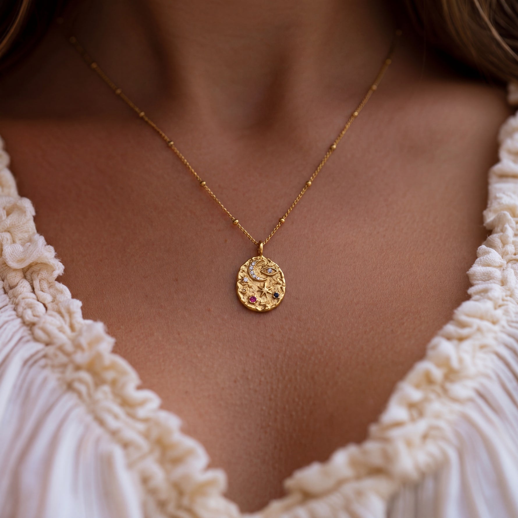 Gold necklace with a pendant worn by a person in a white lace top.
