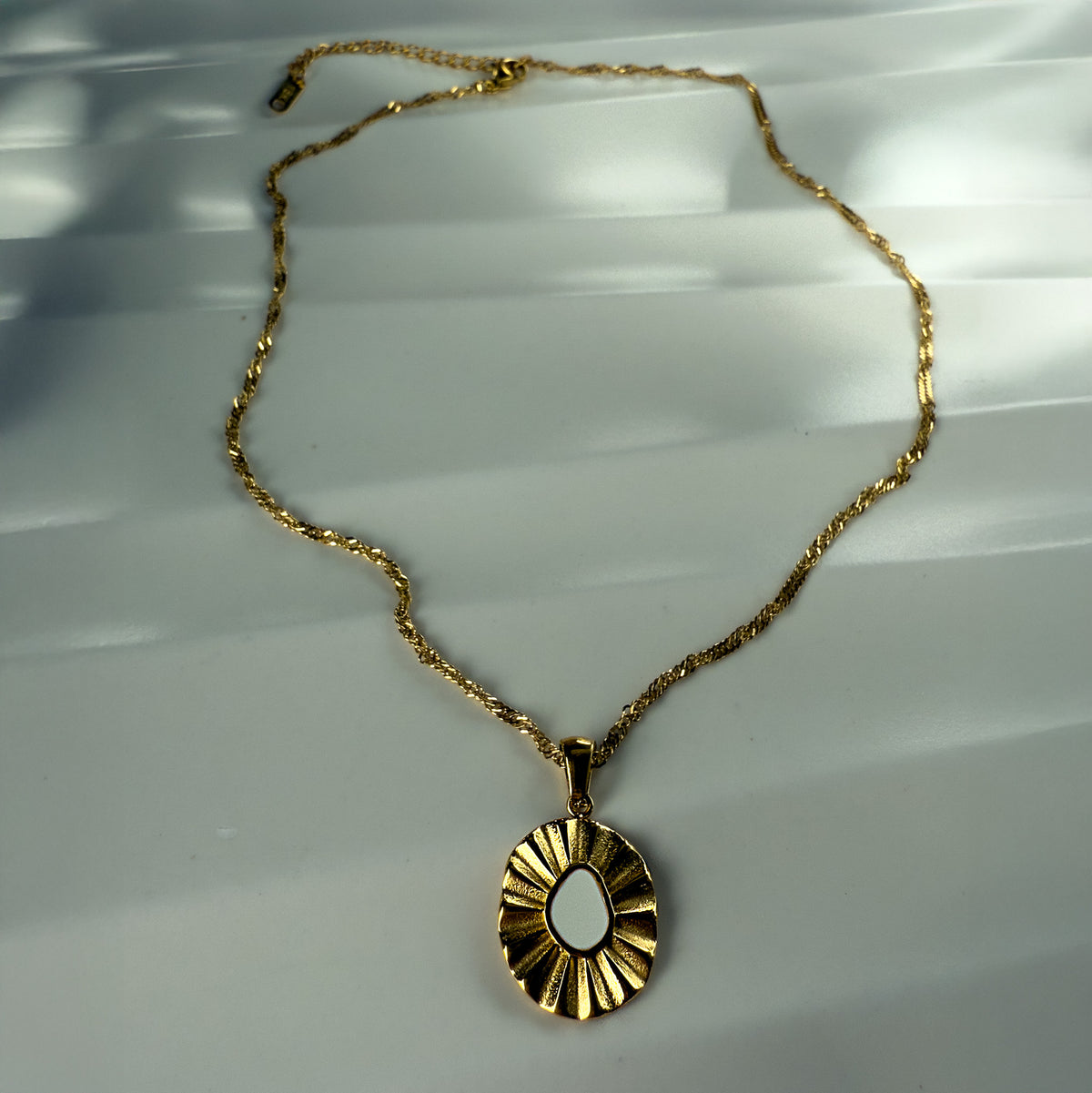 Full view of the Elara white enamel flower necklace with twisted gold chain, shown on a soft porcelain surface in natural light.