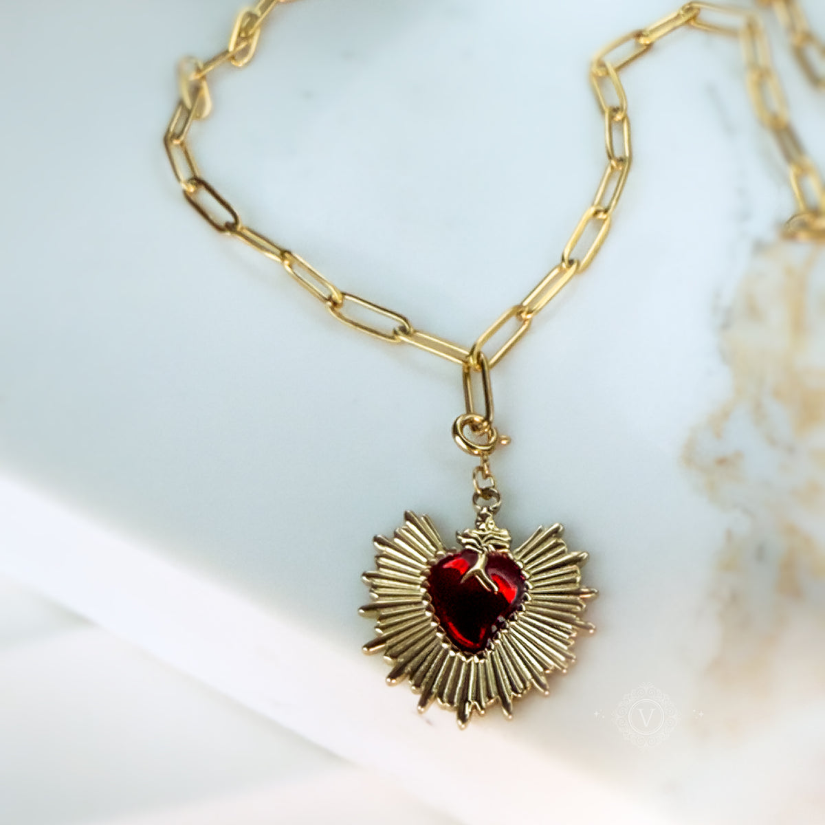Focused front view of the Eloria Sacred Heart pendant with gold rays and deep red enamel on a golden chain.

