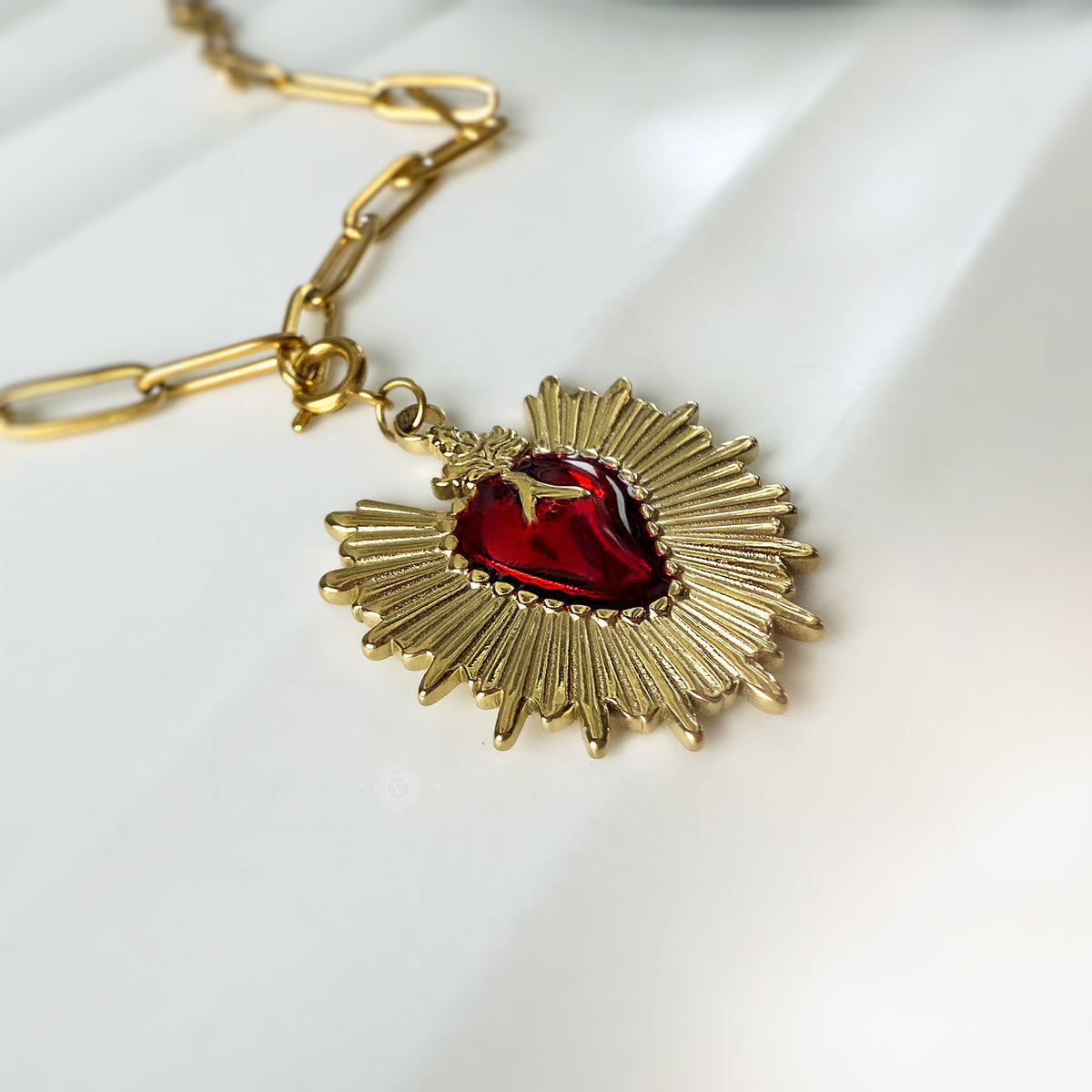 Side angle of the Eloria pendant with reflections of light on the red enamel and gold-tone chain.