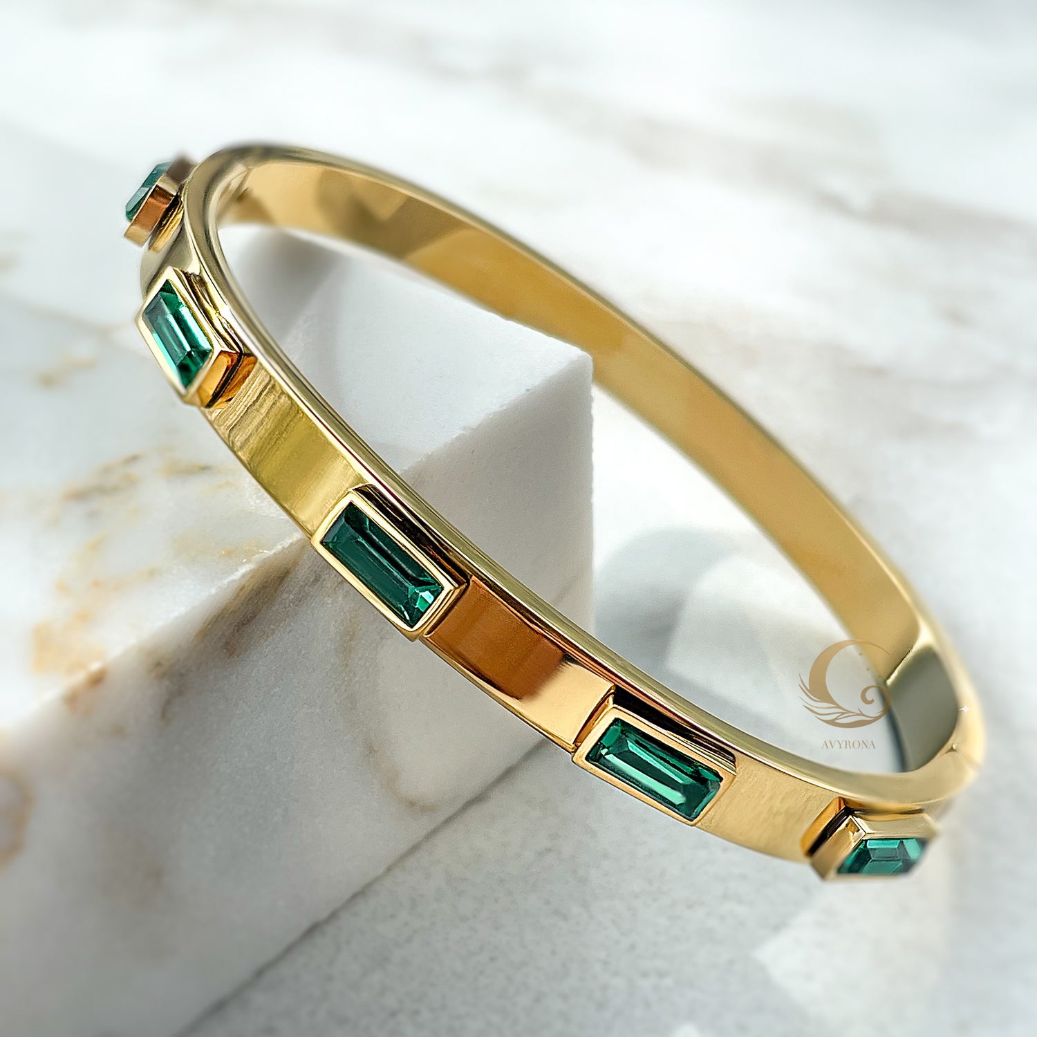 Close-up side view of emerald crystal gold bangle bracelet, highlighting its glossy finish and stone detailing.