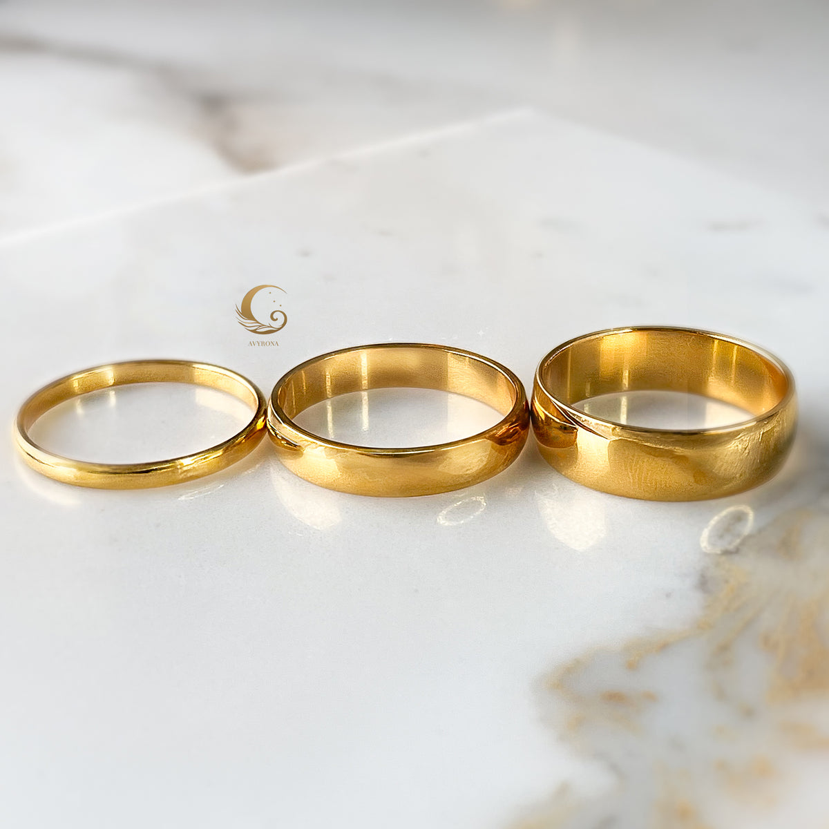 Three gold bands aligned side by side in increasing width order on bright stone surface.