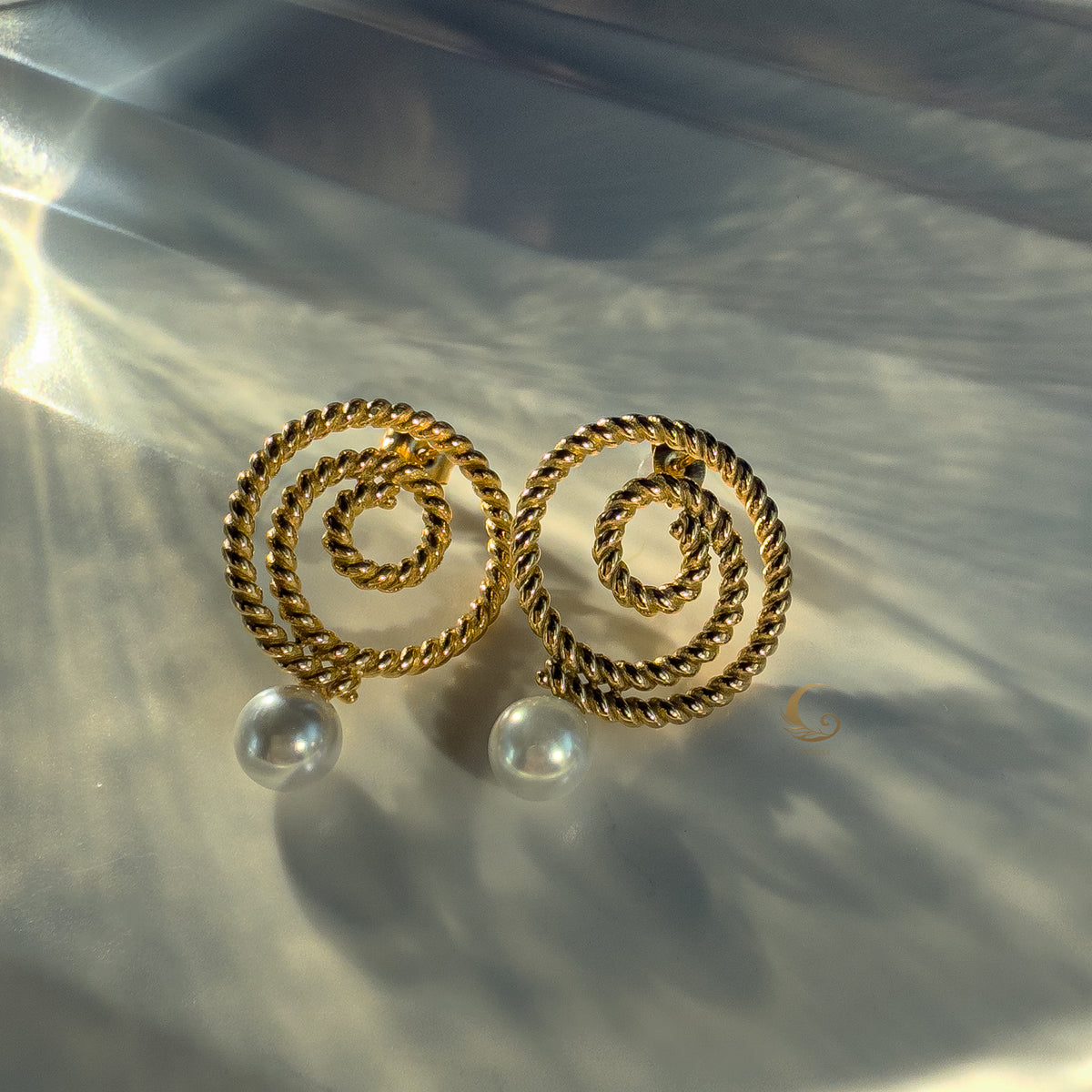 Gold Thaleia earrings with twisted spirals and pearl-like drops, shining in soft light