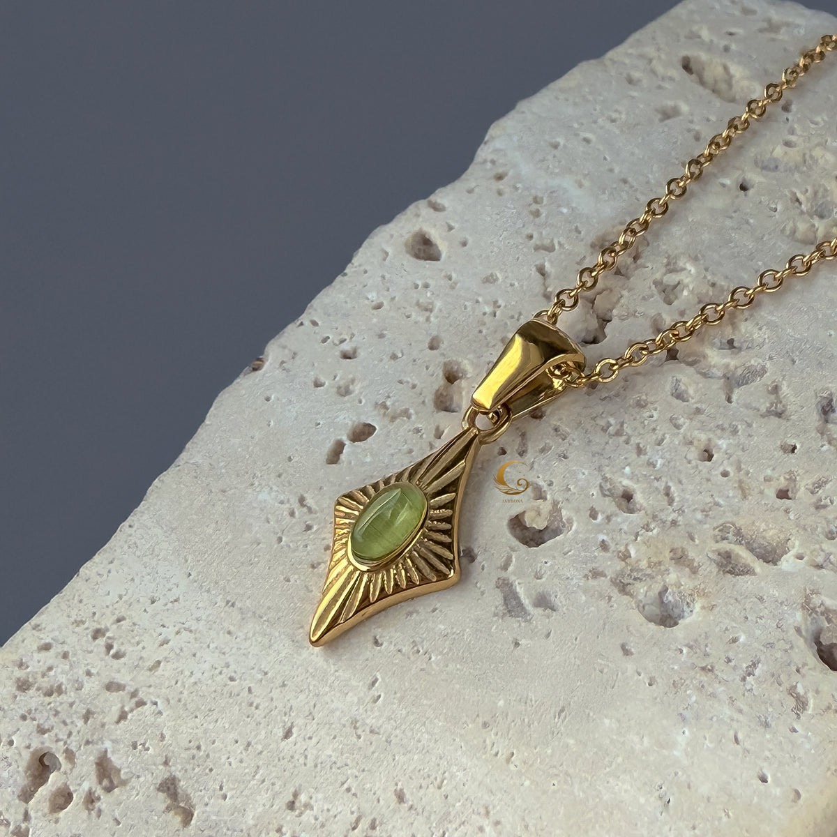  Close-up of the Guardian Amulet necklace with a green cat eye stone, displayed on a light beige textured stone. 