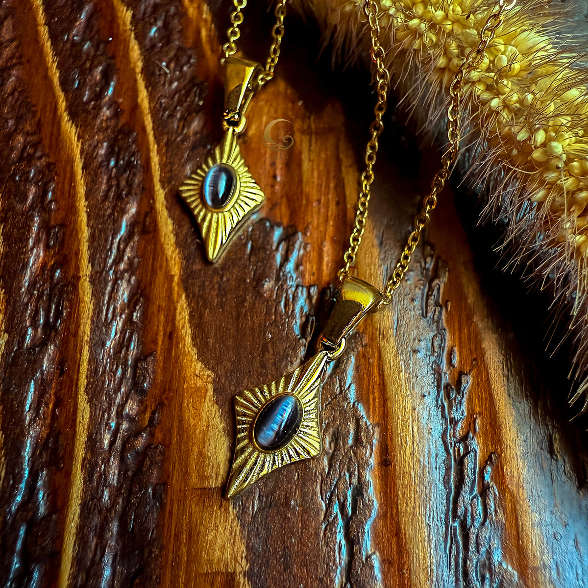 Two Guardian Eye necklaces with black cat eye stones on gold chains, shown on a dark wooden textured background with golden accents.