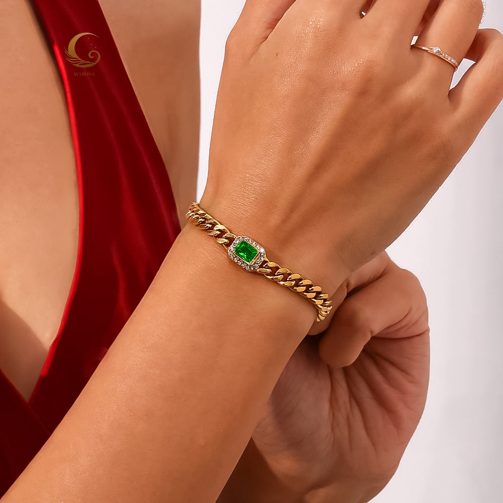Harper Bracelet worn on wrist with red dress, showcasing gold cuban chain and vivid green crystal in natural light.