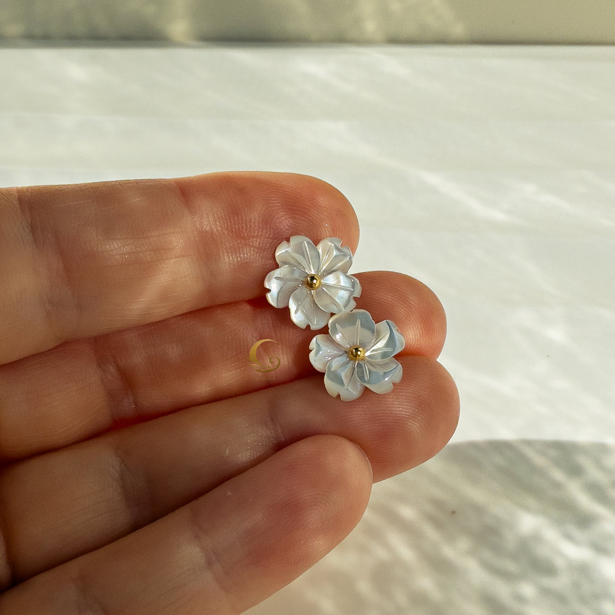  Imira earrings held in hand from above, natural shell flowers with gold-plated centers