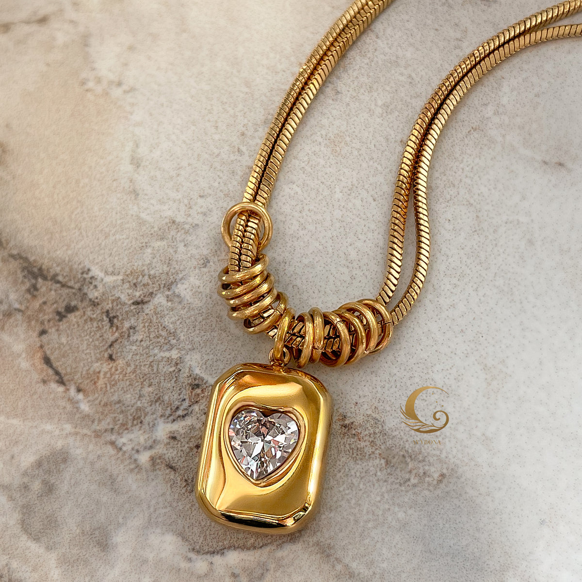 Bold heart-shaped pendant with crystal set in gold, arranged on stone-textured surface.