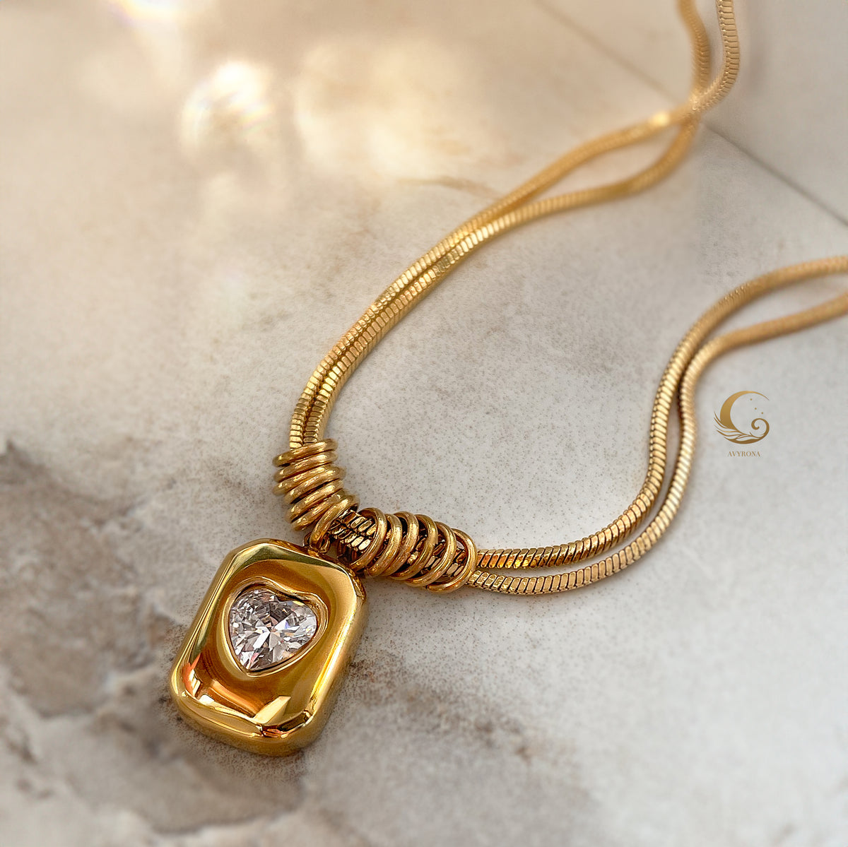 Curved snake chain necklace with heart pendant displayed in soft lighting on warm-toned background.