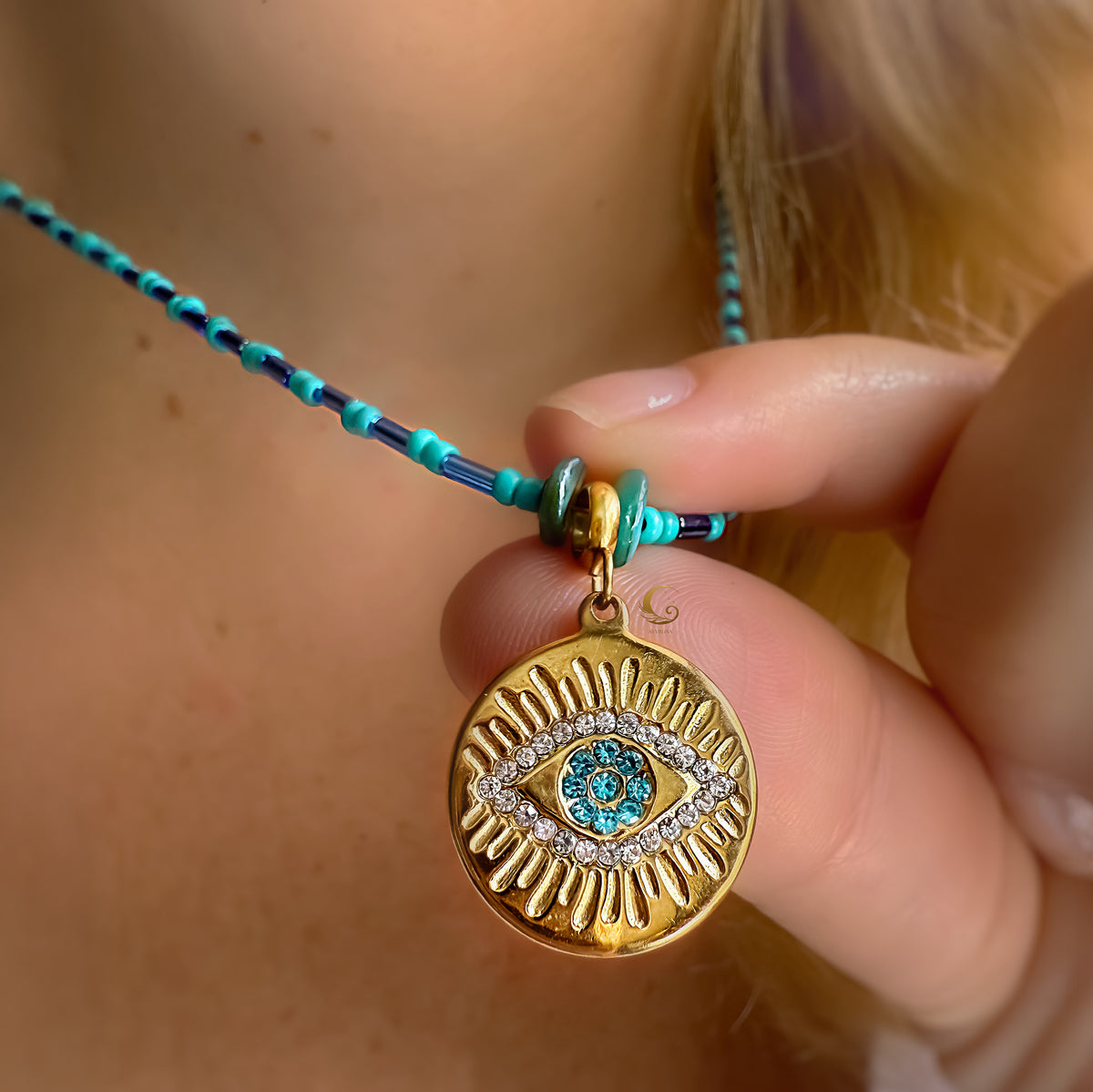 Hand holding the Marisel turquoise Evil Eye necklace showing pendant details and glossy turquoise beads.