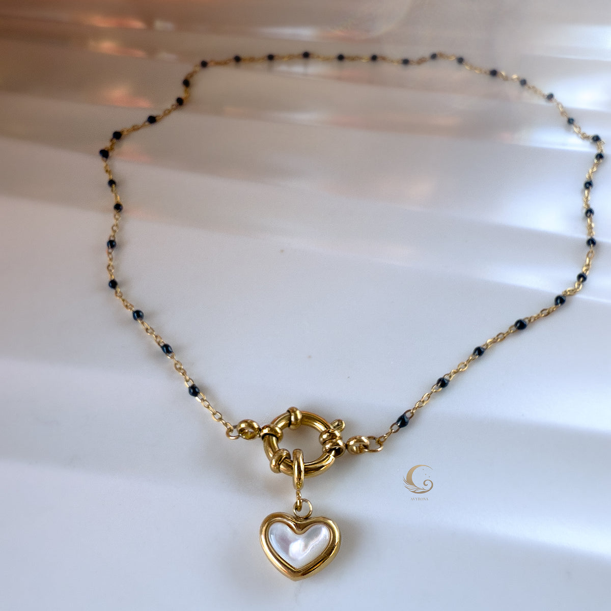  Full view of navy beaded necklace with gold heart charm, displayed in a soft circular shape on white background.