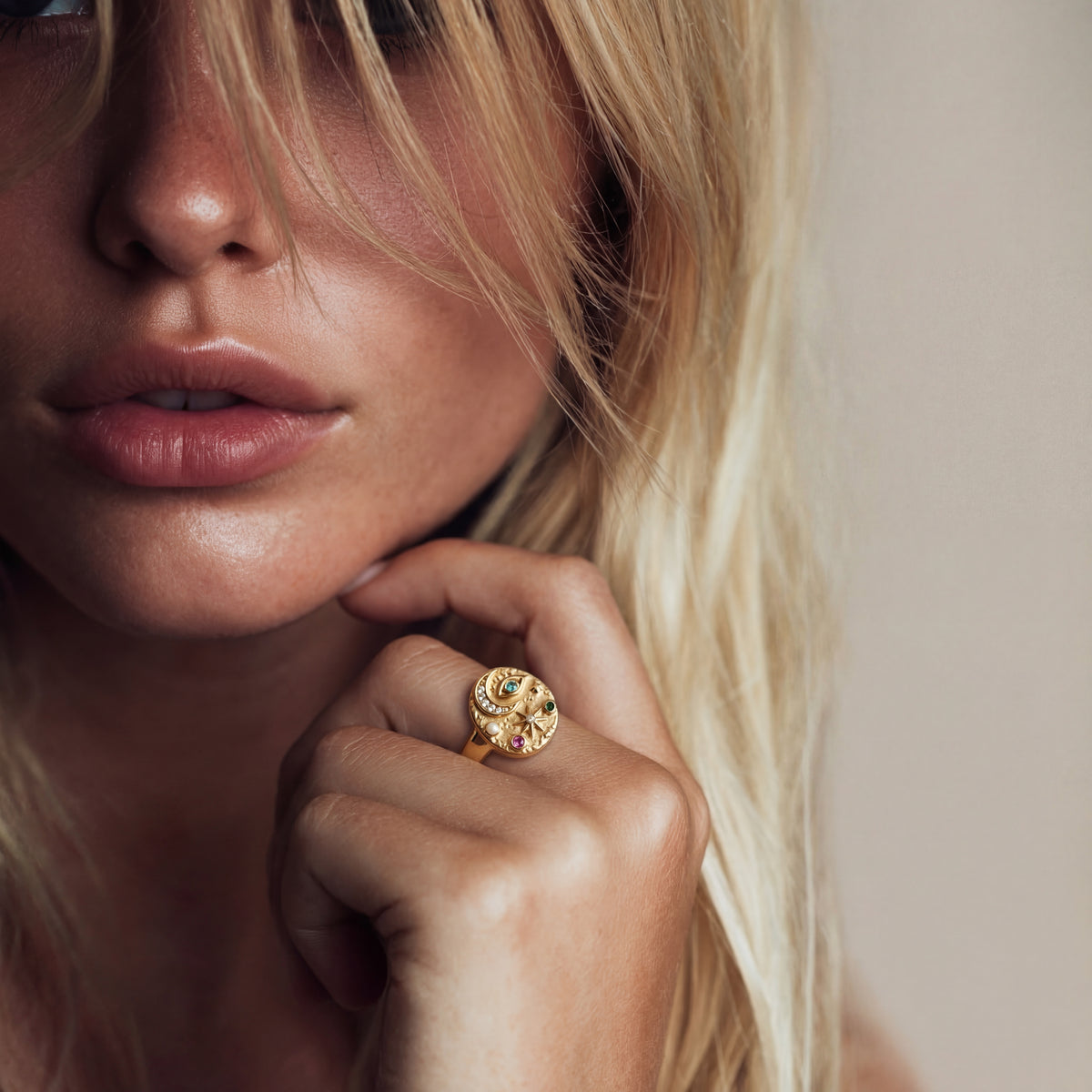 Close-up of a woman wearing a gold ring with a gemstone, against a neutral background.